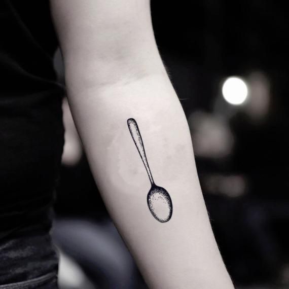 a black and white photo of a spoon tattoo on the left arm, with an outline of a spoon in it