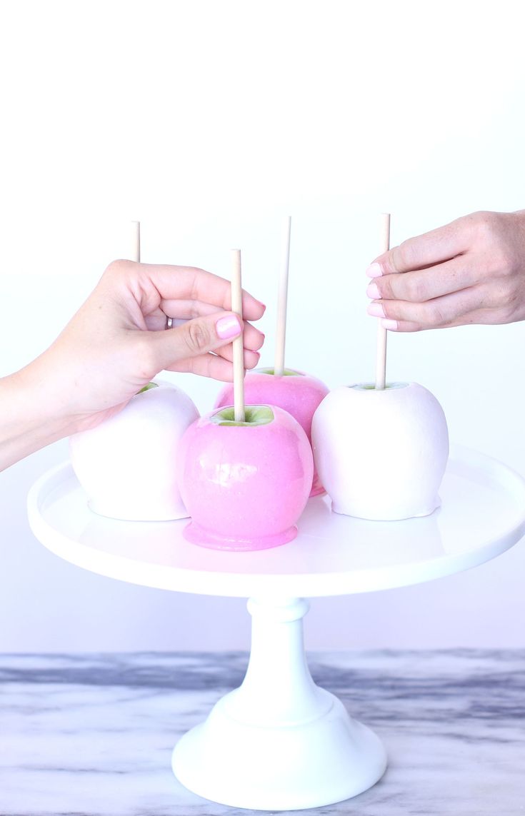 two hands are holding apples on a white cake plate with toothpicks in them