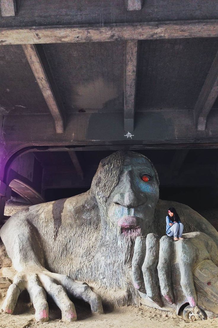 two people are standing next to a giant creature in the dirt under a bridge with purple lights