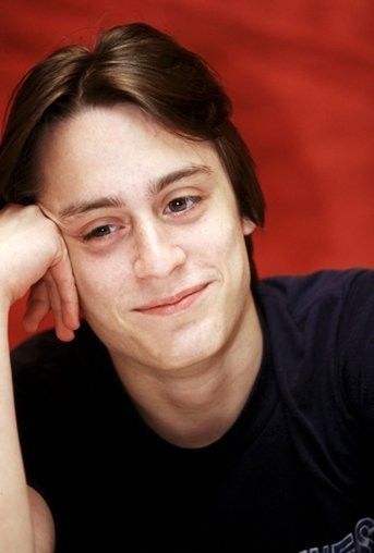 a young man sitting down with his hand on his head and looking at the camera