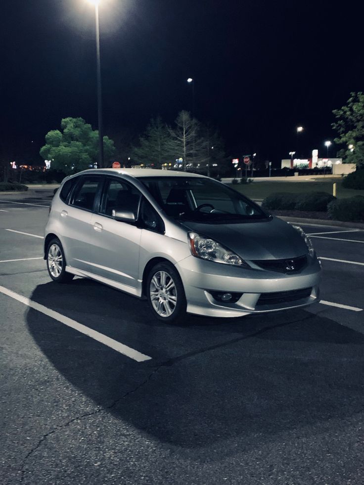 a small silver car parked in a parking lot at night with street lights above it