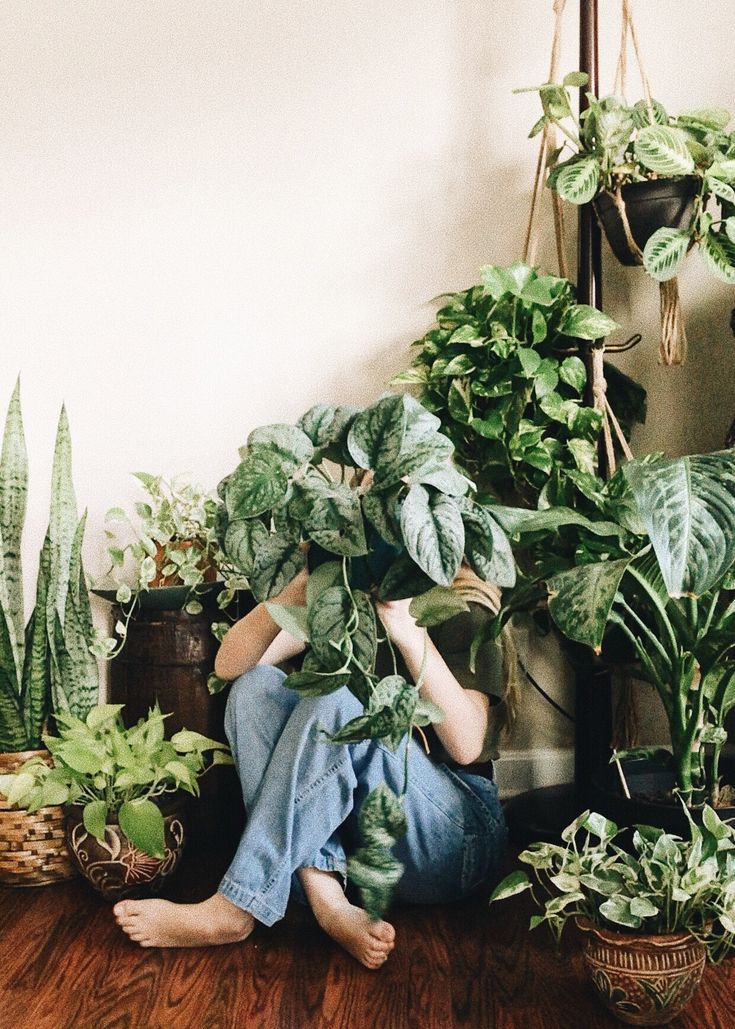 a woman sitting on the floor surrounded by potted plants