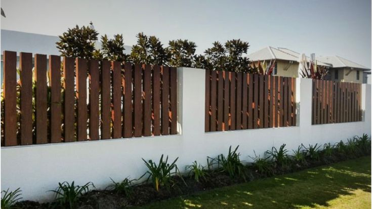 a white fence with wooden slats on it and grass in the front yard area