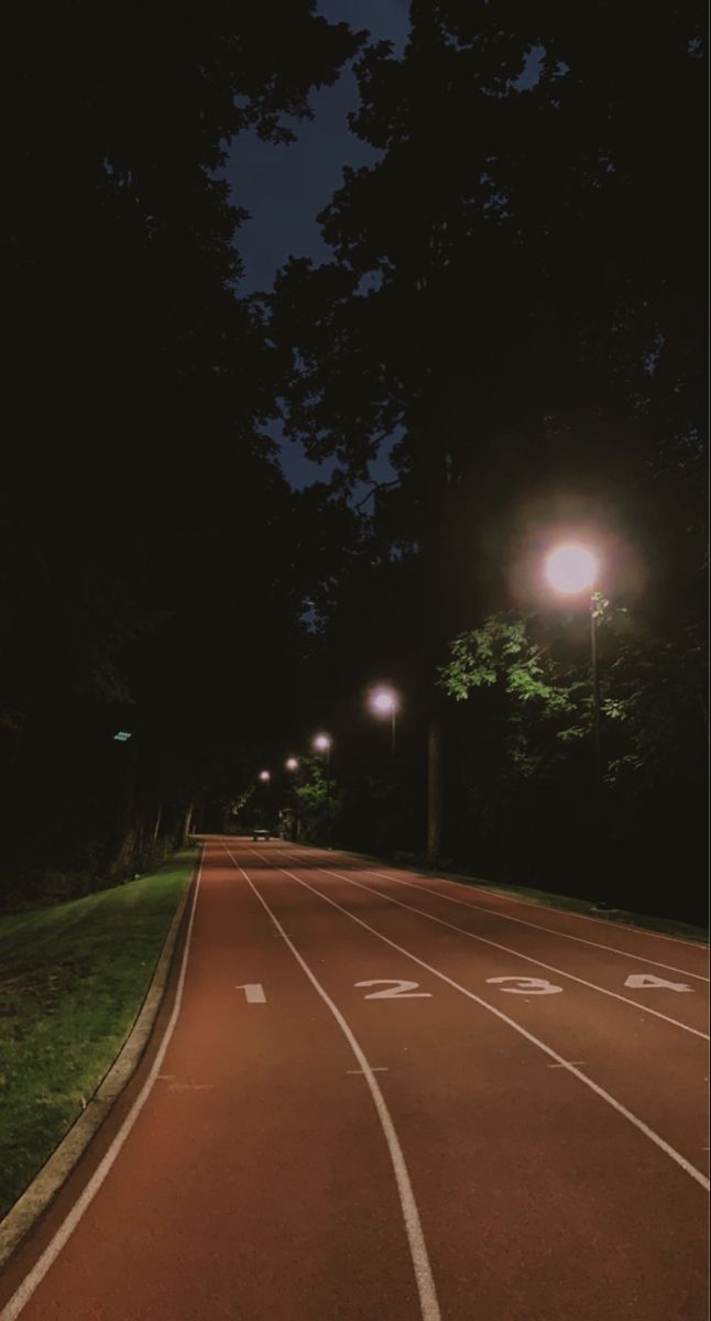 an empty road at night with street lights on the side and trees in the background