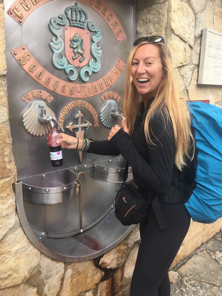 a woman standing in front of a metal sign with a bottle of booze on it