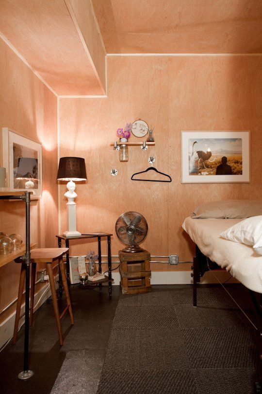 a bedroom with a bed, fan and two tables in front of the room's walls