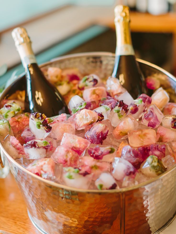 two bottles of champagne are sitting in an ice bucket filled with pink and white flowers