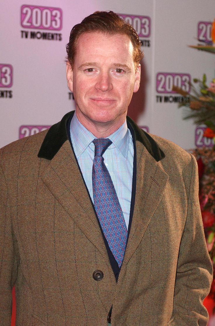 a man wearing a suit and tie standing in front of a red carpeted wall