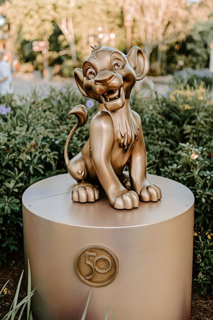 a statue of a lion sitting on top of a round base in front of bushes