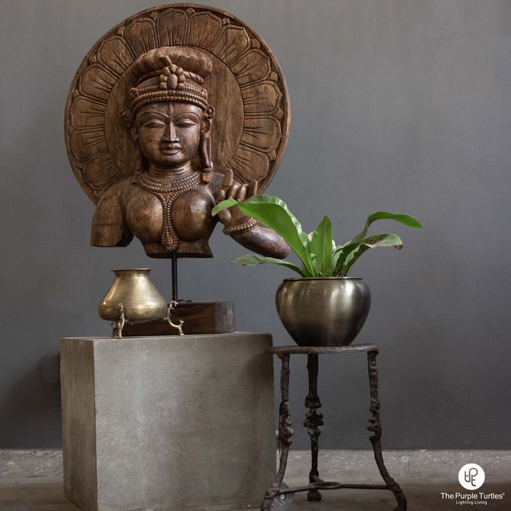 a buddha statue sitting next to a potted plant on a small table in front of a gray wall