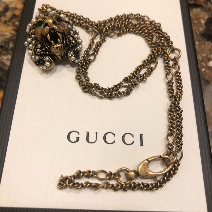 An Essential Design Of The House, The Gucci Lion Head Pendant Necklace Is Embellished With Glass Pearl Beads Along The Mane, And Green Crystals Encrusted In The Eyes. Part Of The Fascination For Lavish Nature And Wild Animals That Nourishes The Gucci Narrative, The Snarling Creature Is Fashioned From Metal With An Aged Gold Finish. New In Box Gucci Lion Head Pendant Necklace Antique Gold Necklace With Pendant Lion Head Lobster Clasp Closure 11.5" Chain Adjustable To 9.5" 1" X .75" Pendant Produc Designer Jeweled Jewelry Gift, Vintage Gold Gucci Jewelry, Vintage Gucci Gold Jewelry, Vintage Gucci Jewelry For Formal Occasions, Vintage Gucci Jewelry For Formal Events, Vintage Necklace With Logo Charm For Formal Occasions, Luxury Jeweled Necklaces For Formal Occasions, Luxury Jeweled Necklace For Formal Occasions, Gucci Luxury Pendant Necklace