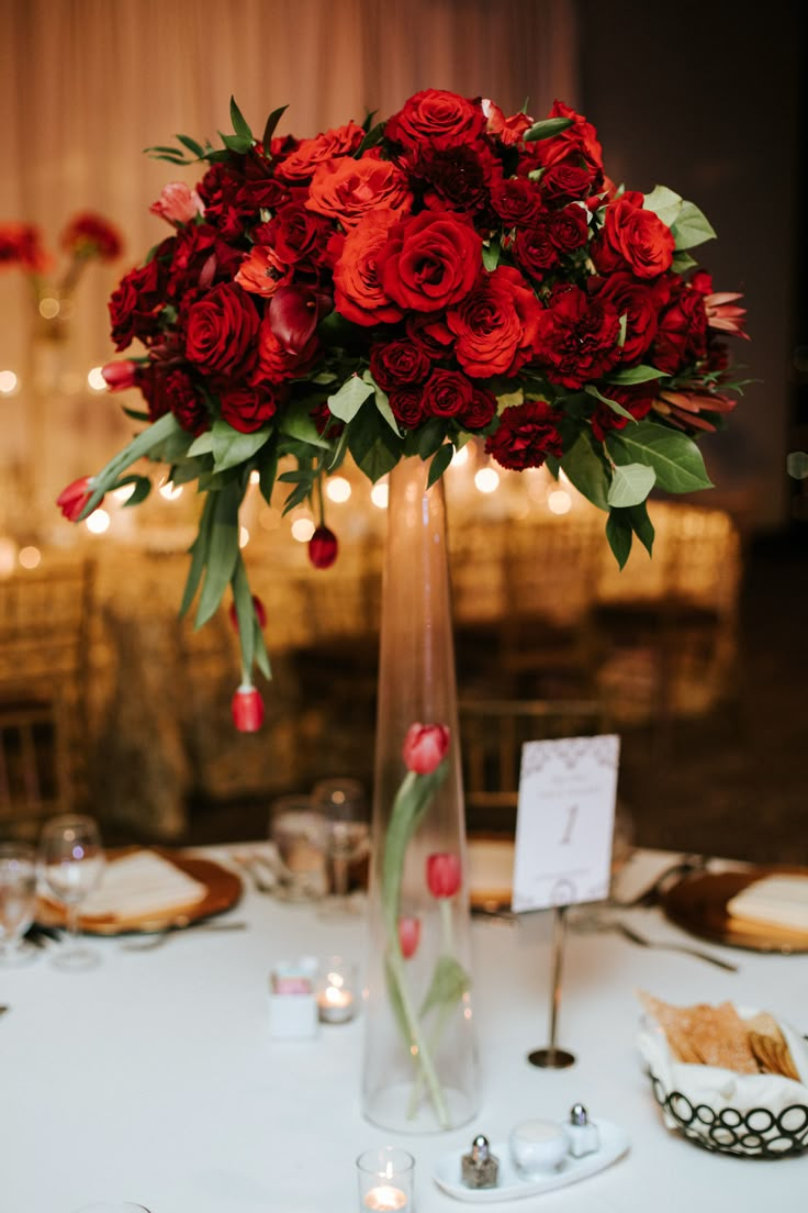 a tall vase filled with red flowers on top of a white tablecloth covered table