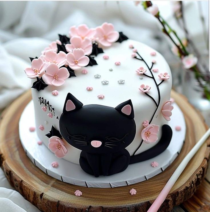 a white cake decorated with black cat and pink flowers on a wooden platter next to a knife