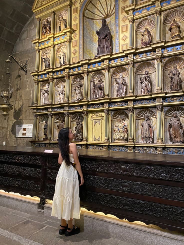 a woman standing in front of a wall with paintings on it's sides and an altar behind her