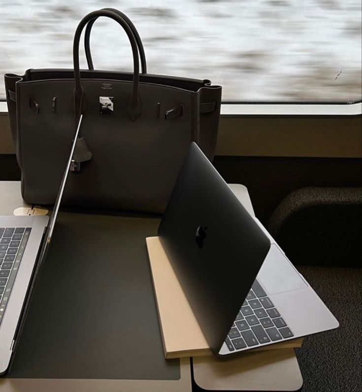 an open laptop computer sitting on top of a desk next to a bag and purse