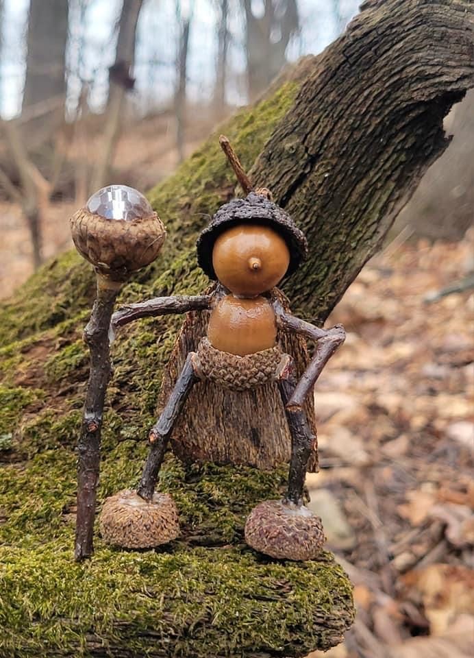 a small wooden figure sitting on top of a moss covered log