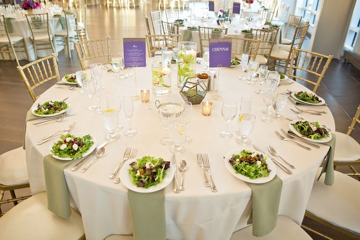 the table is set with white linens, silverware and green salad on it