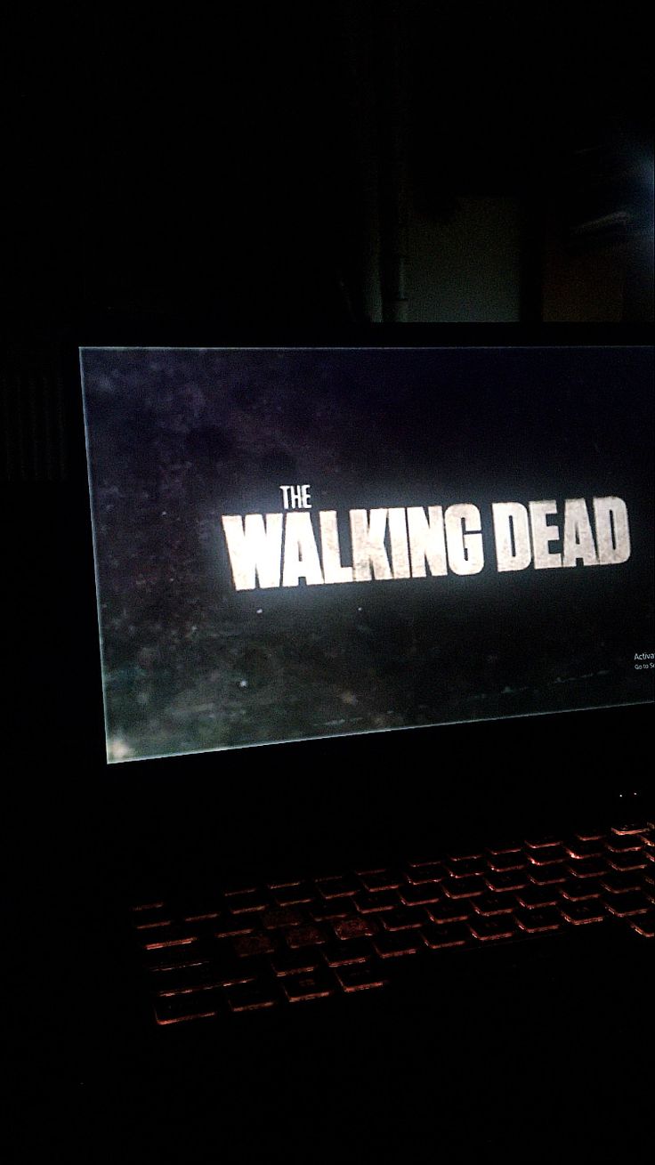 the walking dead logo is projected on a computer screen in the dark with red light coming from behind it