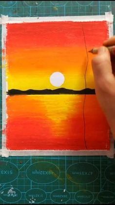 someone is painting an orange and yellow sunset on a piece of paper with a pencil