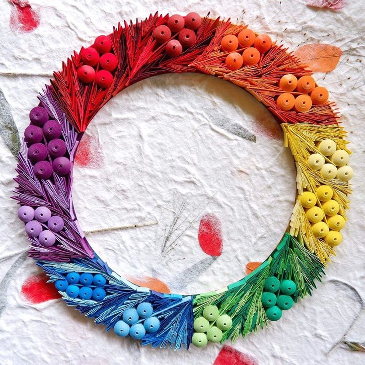 a colorful wreath made out of buttons and feathers on a white surface with red, orange, yellow, green, blue and purple colors