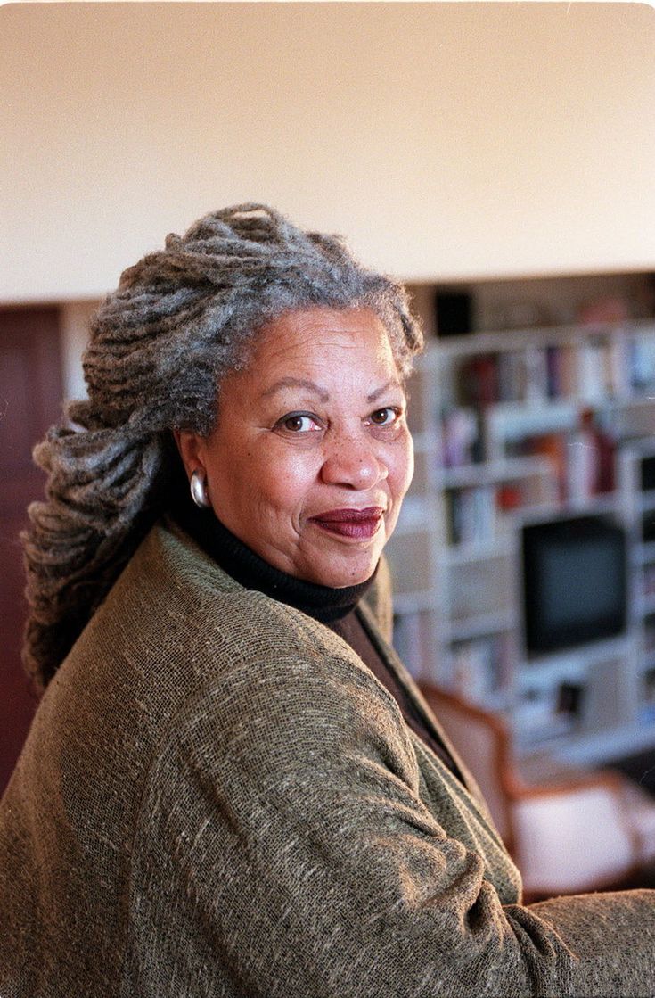 an older woman with dreadlocks smiles at the camera in front of a bookshelf