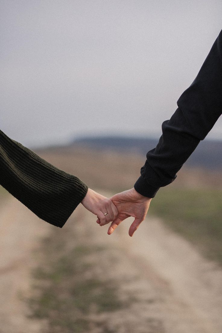 two people holding hands while walking down a dirt road