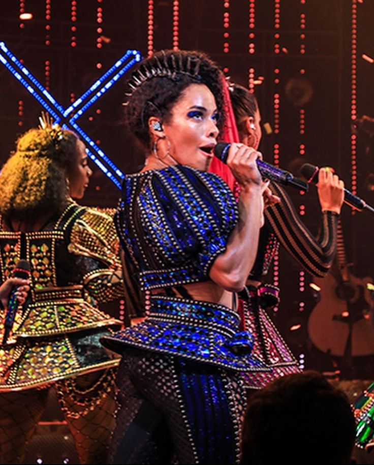 a group of women on stage with microphones in their hands and lights behind them