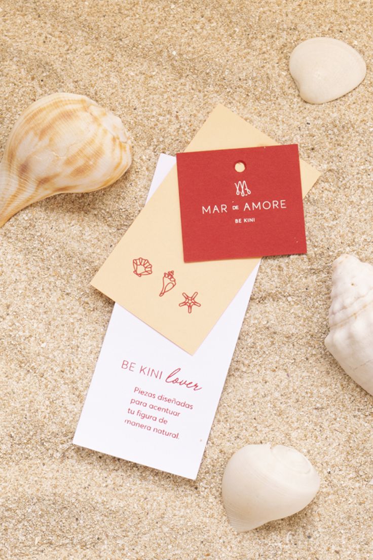 some sea shells are laying on the sand and there is a red card that says mar d'more