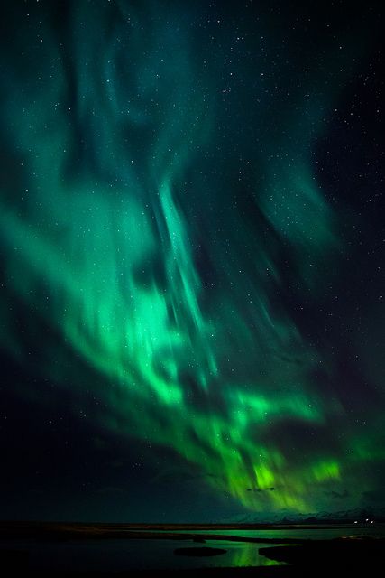 green and purple lights shine in the night sky above an ocean with calm water below