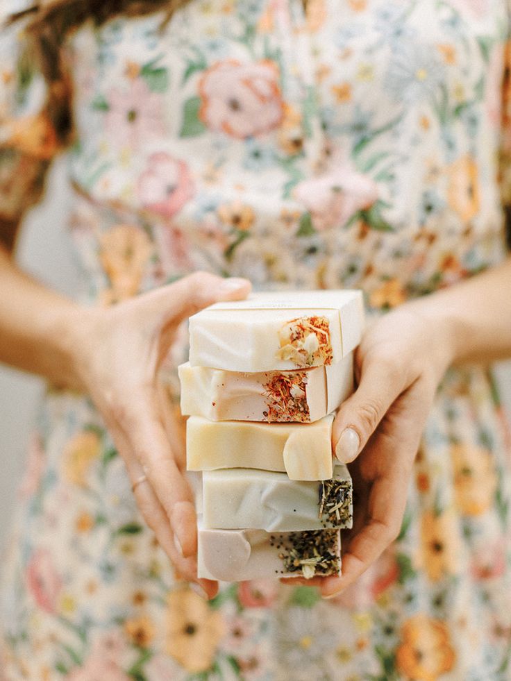 a woman holding three different types of soaps in her hands with flowers on them