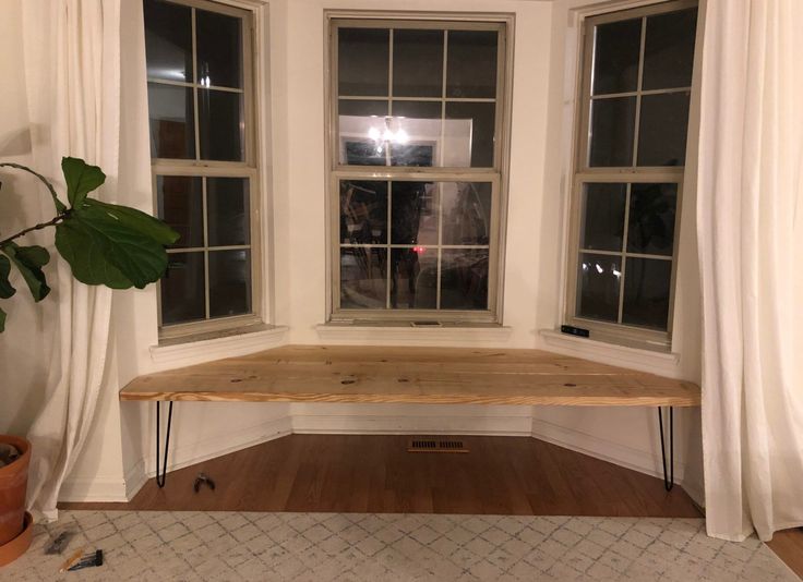 a wooden bench sitting in front of two windows next to a rug and potted plant