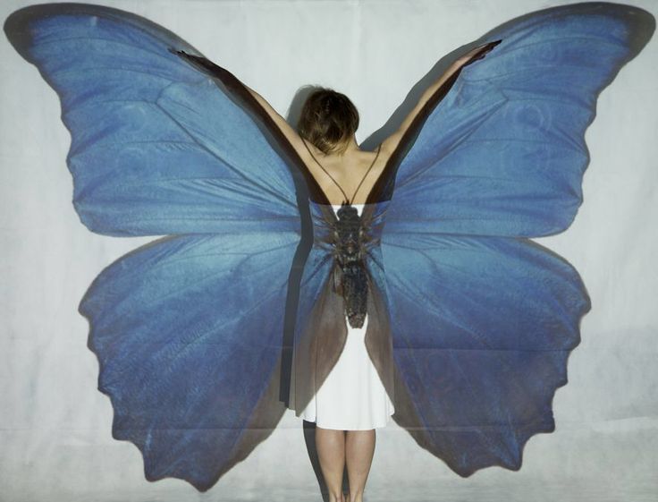 a woman in a white dress with a blue butterfly on her back and wings spread out