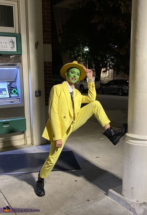 a man in a yellow suit and green face paint posing for a photo on the sidewalk