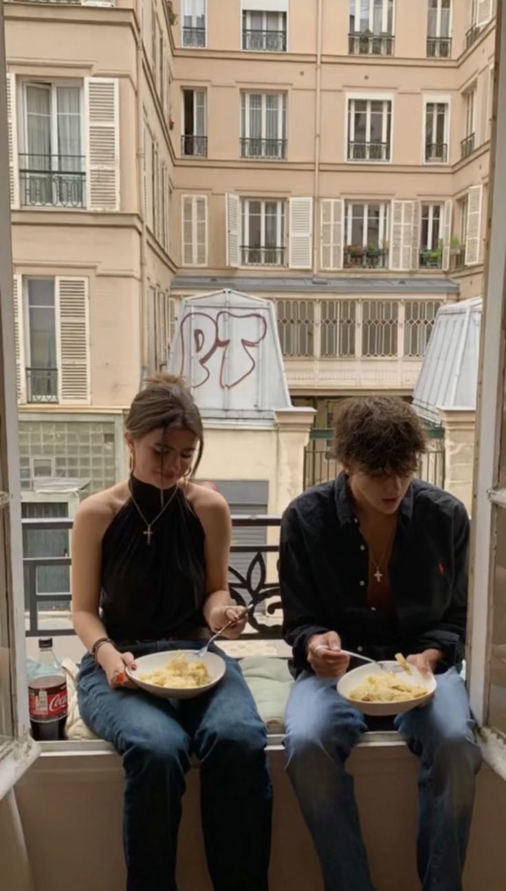 two people sitting on a window sill with plates of food in front of them