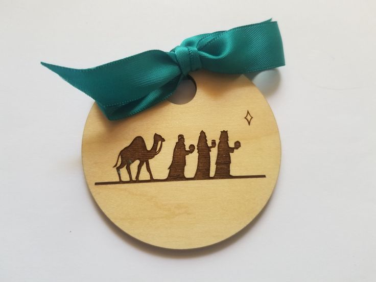 a wooden ornament with three wise men and a camel on it, hanging from a green ribbon