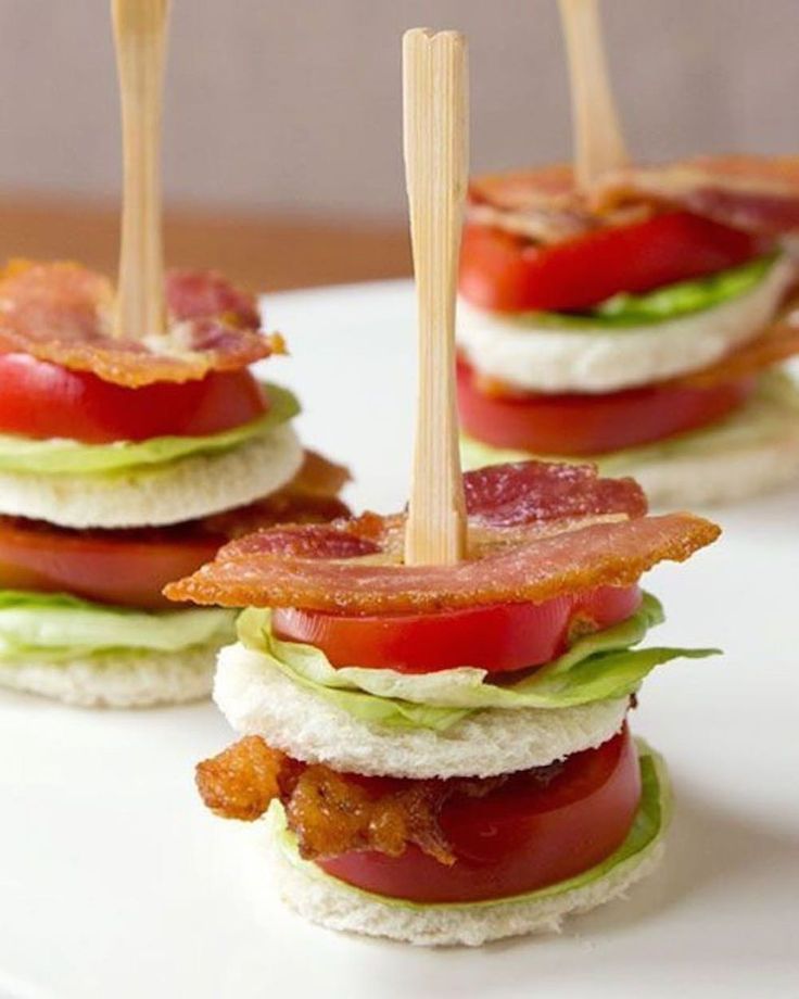 mini sandwiches with bacon, lettuce and tomato on them sitting on a white plate