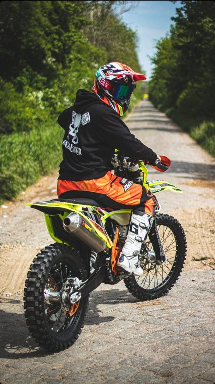 a man riding on the back of a dirt bike down a road next to trees