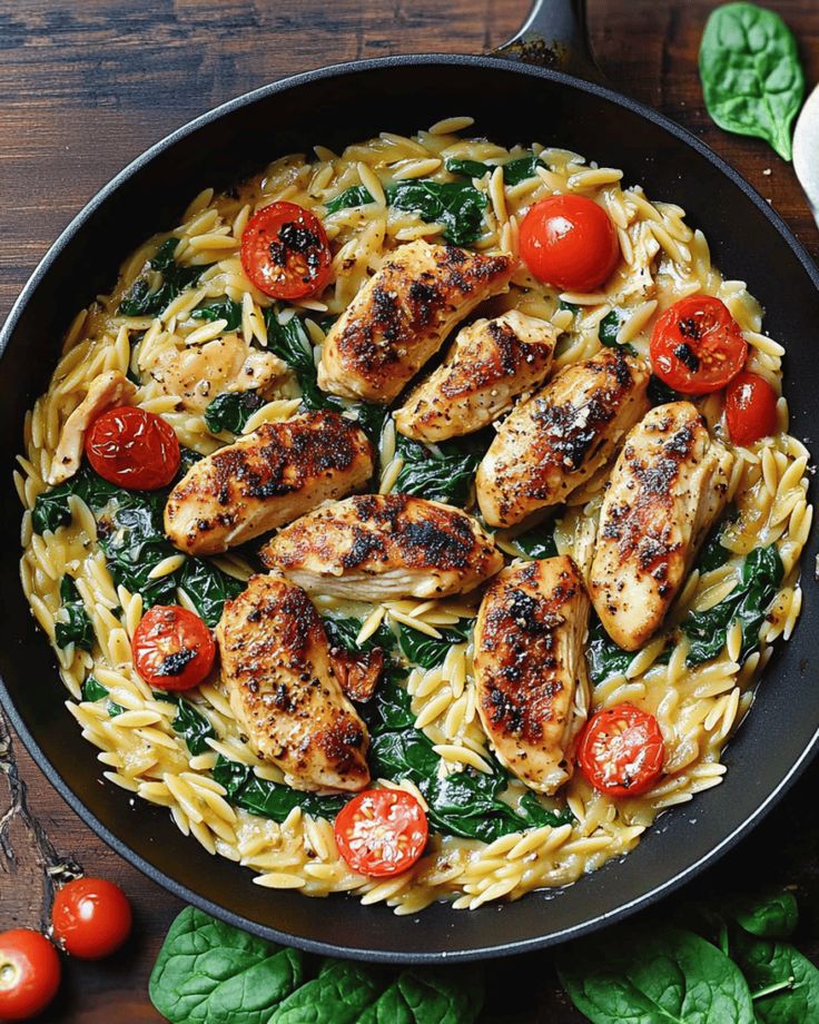 chicken and spinach pasta in a skillet on a wooden table next to tomatoes