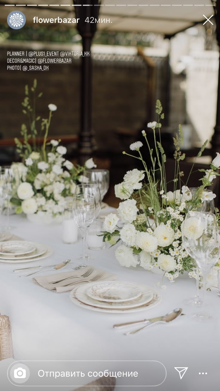 the table is set with white flowers and place settings