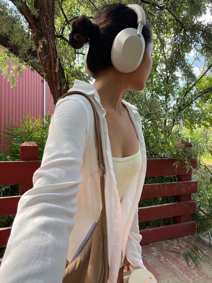 a woman with headphones is sitting on a bench and looking at the trees in front of her