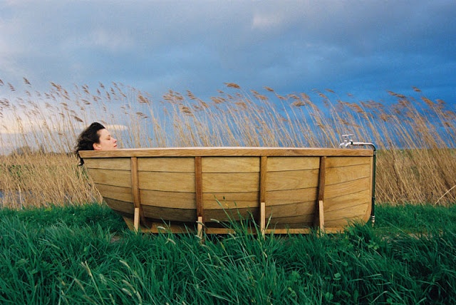 a woman is sitting in a wooden boat on the grass and looking at the water