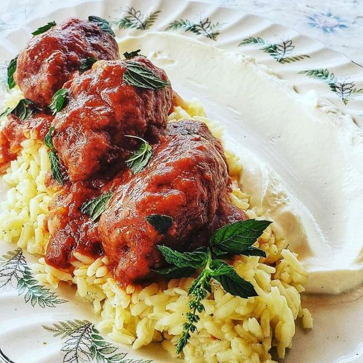 two meatballs covered in sauce and rice on a white plate with green sprigs