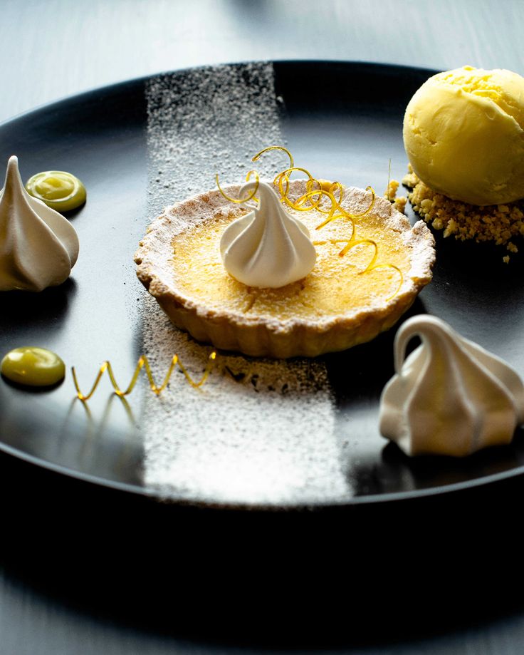 three desserts are on a black plate with white icing and yellow toppings