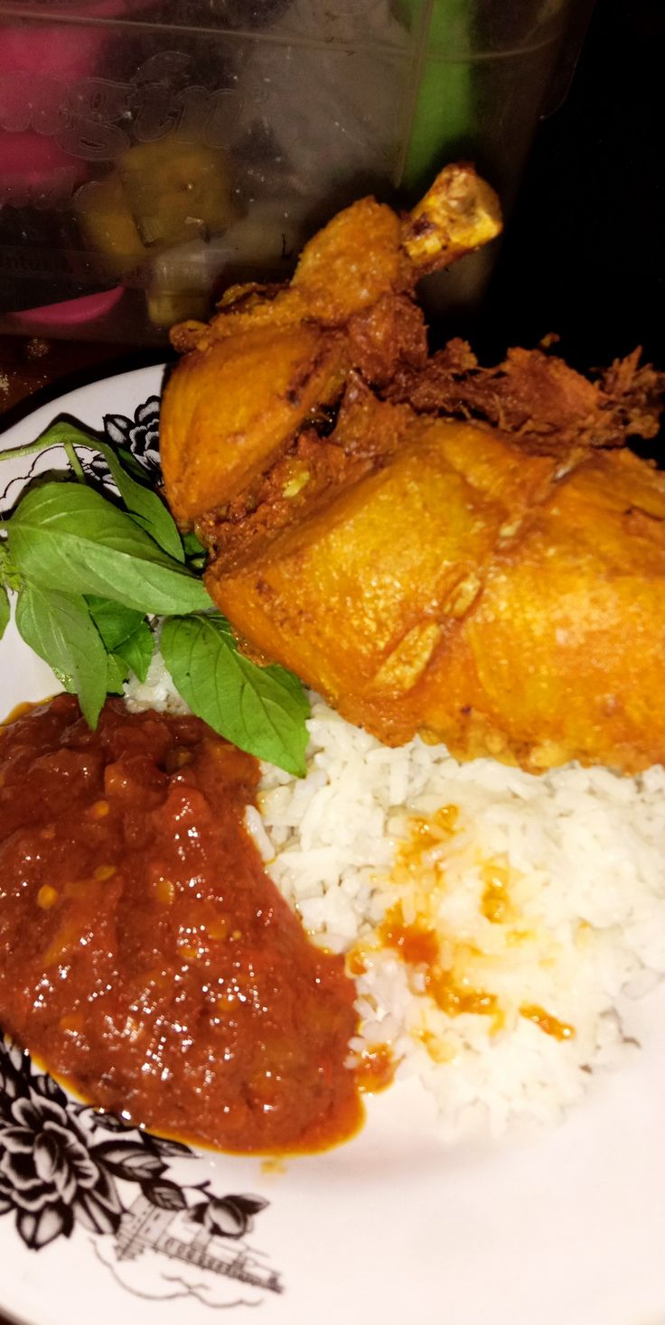 a white plate topped with rice and meat covered in sauce next to green leafy garnish