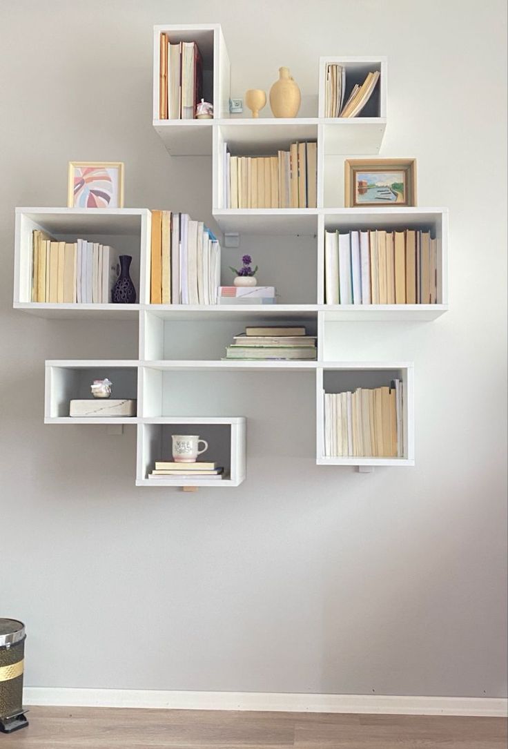 a white shelf filled with lots of books on top of a wooden floor next to a wall