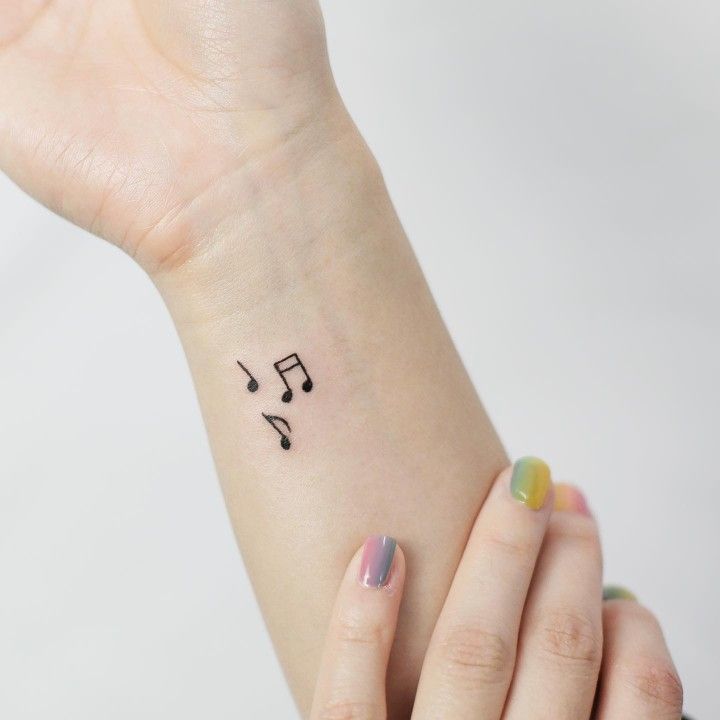 a woman's wrist with musical notes tattooed on the left side of her arm