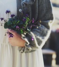 a woman wearing a white dress holding a bouquet of purple flowers in her right hand