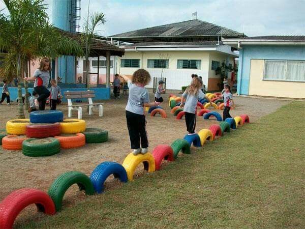 children playing in an outdoor play area with colorful tires and sandbags on the ground