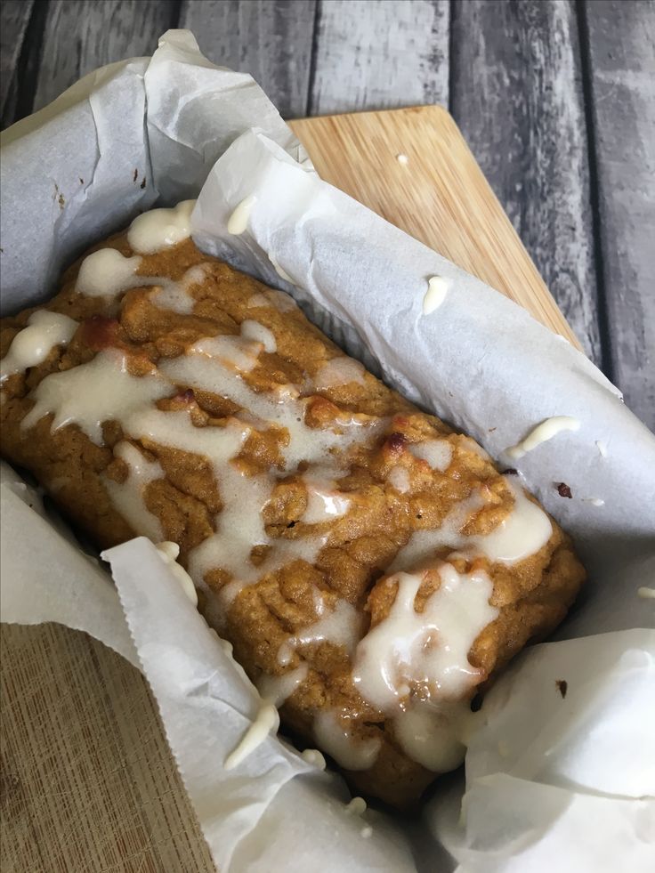 a loaf of bread with white icing on it sitting in a paper wrapper