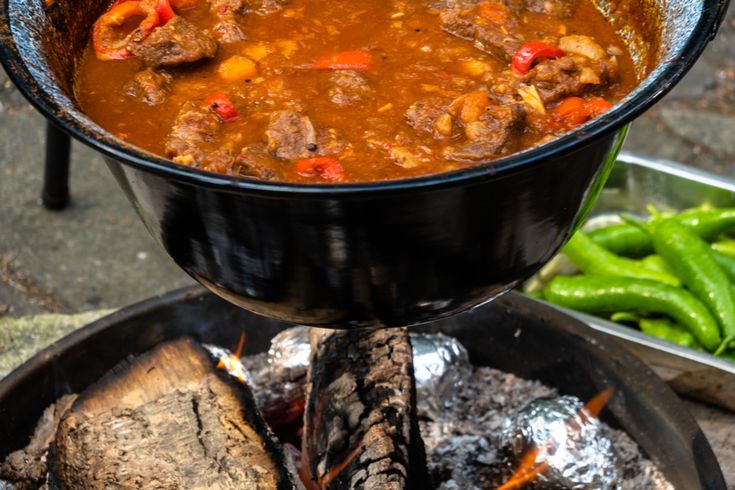 a large pot filled with stew next to some green beans and hotdog buns